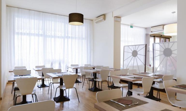 Restaurant moderne avec tables dressées et grandes fenêtres lumineuses.